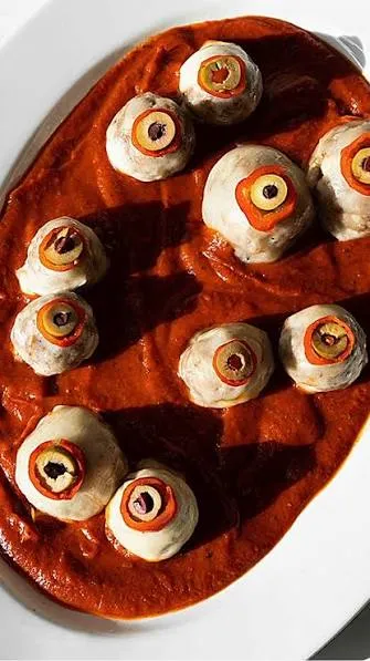 Bowl of spicy meatballs in red sauce, each topped with a mozzarella ball and black olive pupil