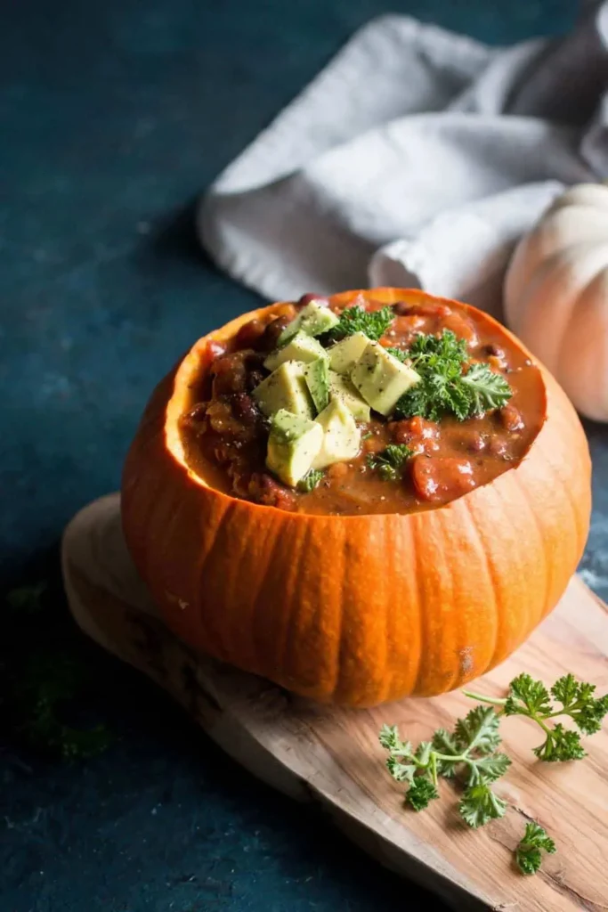 Dark bowl of thick orange pumpkin chili topped with sour cream and green onion